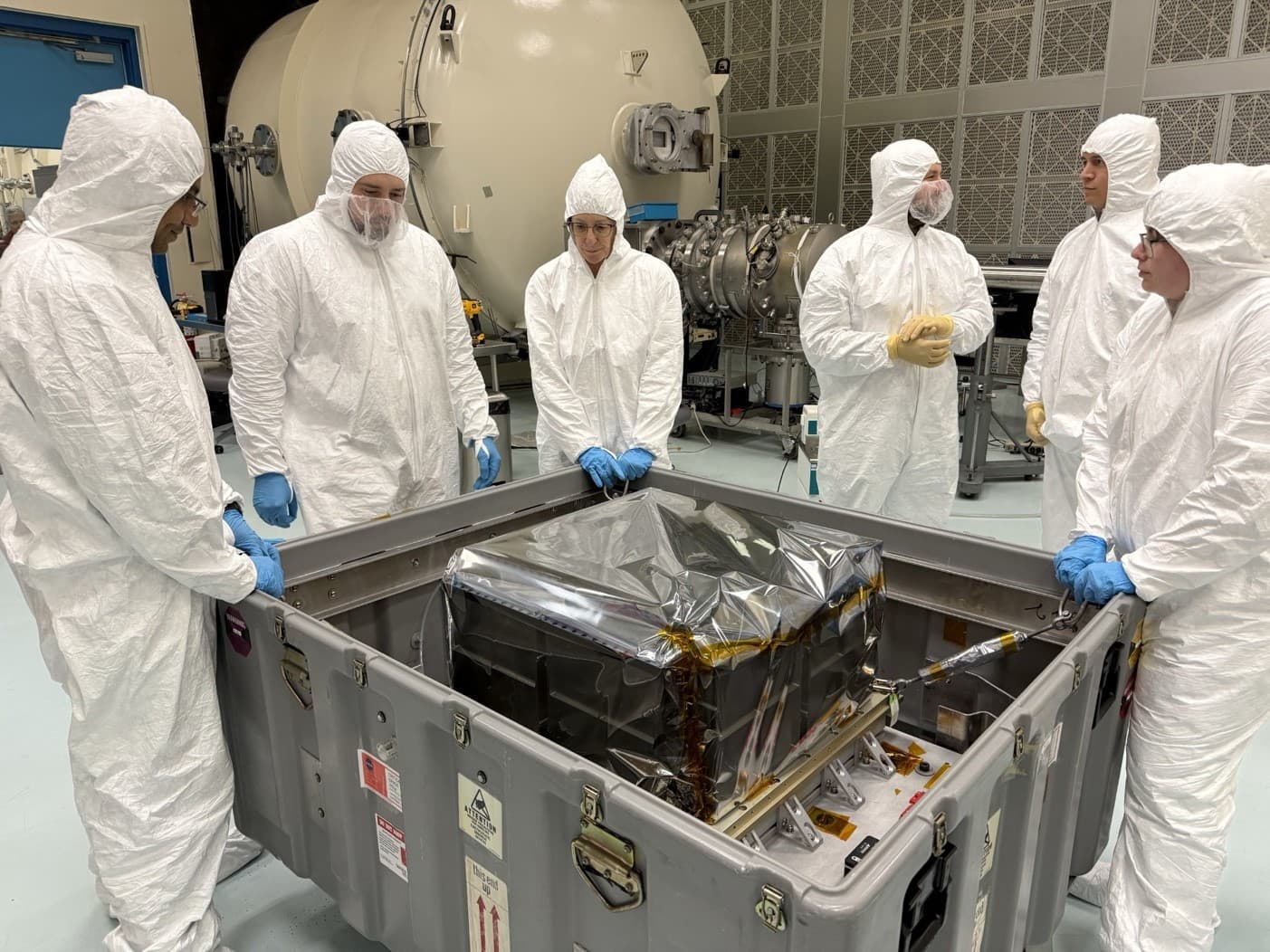 Engineers in cleanroom suits stand around the StarBurst observatory inside a shipping container